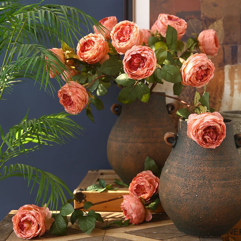 Puede incluir: Un ramo de rosas de seda de color melocot&oacute;n dispuestas en dos macetas de terracota. Las rosas est&aacute;n en plena floraci&oacute;n y tienen un aspecto realista.
