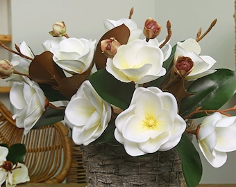 Puede incluir: Un ramo de flores blancas de magnolia con hojas marrones en una cesta tejida. Las flores están dispuestas en un jarrón y están en plena floración.