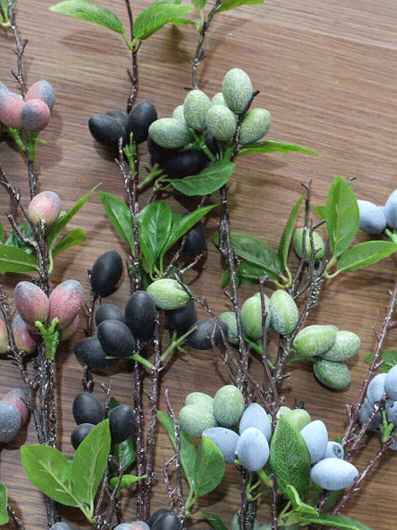 May include: A bunch of artificial berry sprigs with green leaves. The berries are in various colors, including black, green, blue, and pink.