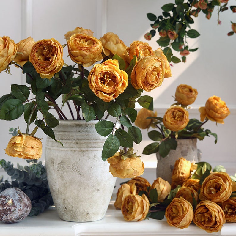 Puede incluir: Un ramo de rosas amarillas artificiales en un jarr&oacute;n de cer&aacute;mica blanco. Las rosas est&aacute;n dispuestas en un estilo suelto y natural y tienen un aspecto realista.