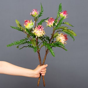 May include: A bouquet of artificial pink and yellow flowers with green leaves. The flowers are arranged in a hand-held bouquet.