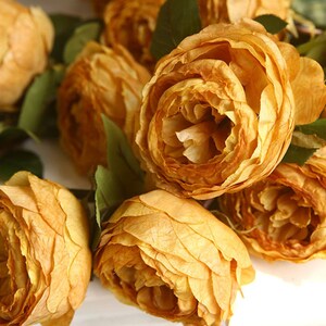 Puede incluir: Un ramo de rosas artificiales de color amarillo intenso y apagado. Las rosas est&aacute;n dispuestas en un racimo, con los p&eacute;talos superpuestos y creando un aspecto suave y texturizado.