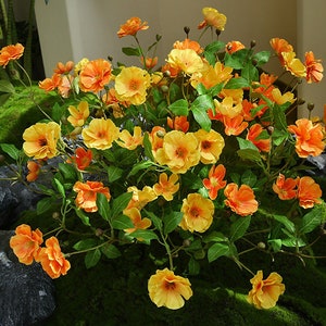 Puede incluir: Un ramo de flores artificiales con pétalos amarillos y naranjas. Las flores están dispuestas en un ramo y tienen hojas verdes.