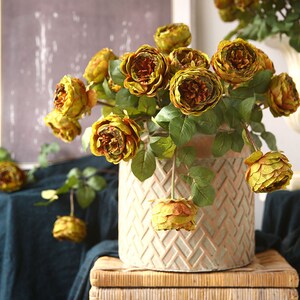 Puede incluir: Un ramo de rosas amarillas artificiales en una maceta de cer&aacute;mica decorativa con un patr&oacute;n tejido. Las rosas est&aacute;n dispuestas en un jarr&oacute;n con hojas verdes.