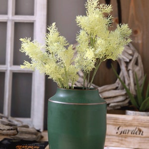 May include: A green ceramic vase with a gold rim, filled with a bouquet of light green artificial dill sprigs.