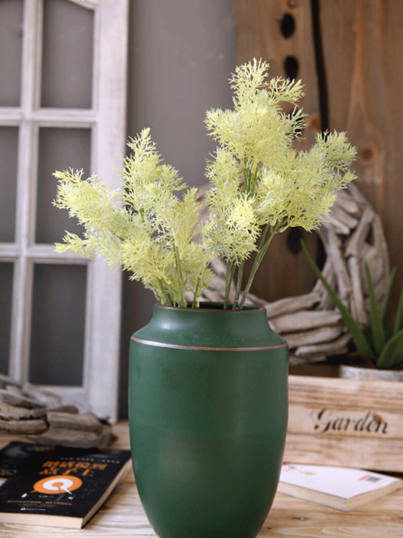 May include: A green ceramic vase with a gold rim, filled with a bouquet of light green artificial dill sprigs.