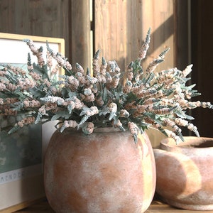 Puede incluir: Un ramo de flores artificiales de color rosa p&aacute;lido y verde en una maceta de terracota. La maceta tiene un acabado blanco desgastado.