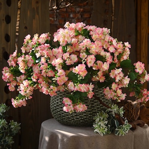 May include: A bouquet of pink and white artificial flowers in a woven basket. The flowers are arranged in a cascading style, creating a lush and full look.