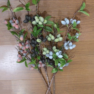 May include: A bouquet of artificial berry sprigs with green leaves. The berries are in shades of blue, green, black, and red.