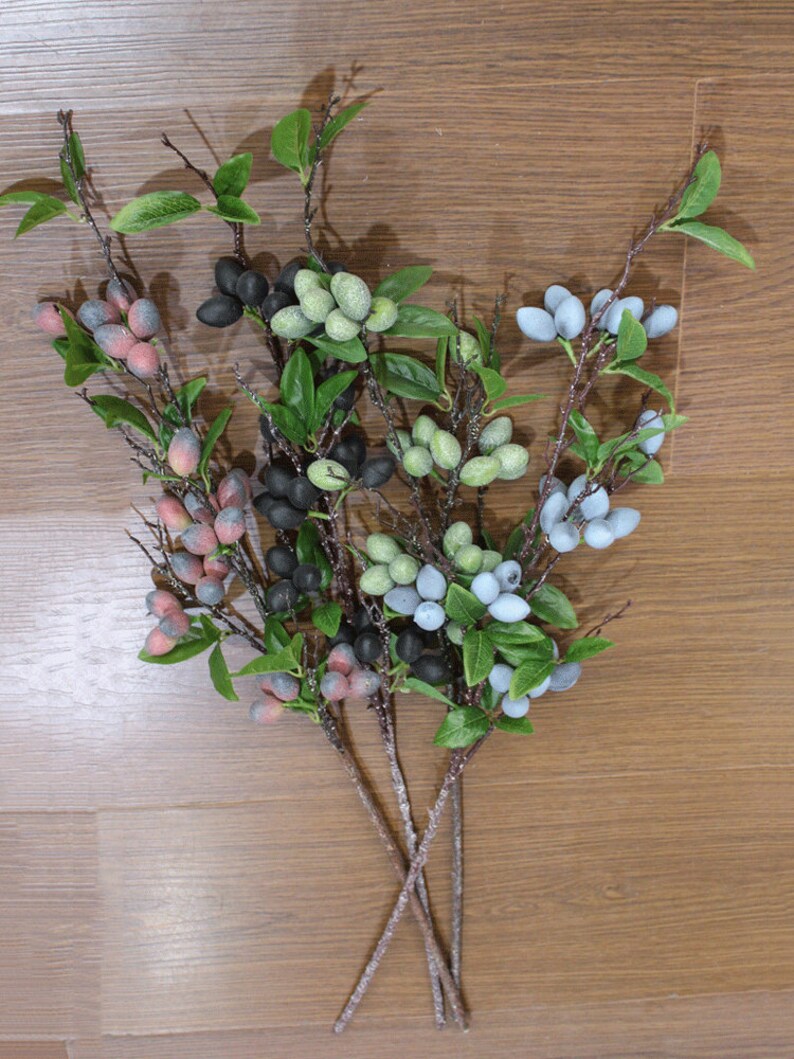 May include: A bouquet of artificial berry sprigs with green leaves. The berries are in shades of blue, green, black, and red.
