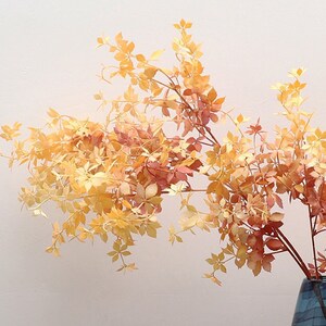 以下が含まれることがあります： 黄色とオレンジの色合いの乾燥した葉が、花瓶に活けられています。葉は繊細で、自然で素朴な外観をしています。