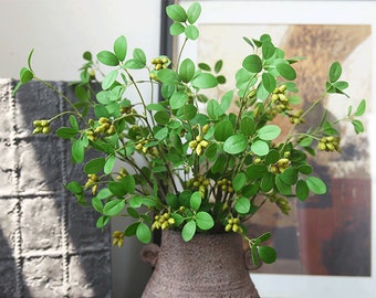 May include: A bouquet of artificial green leaves with small yellow flower buds in a brown ceramic vase.