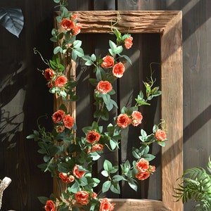 Puede incluir: Un marco de madera con una vid de rosas artificiales de color naranja y hojas verdes. El marco es r&uacute;stico y tiene un acabado de madera natural.