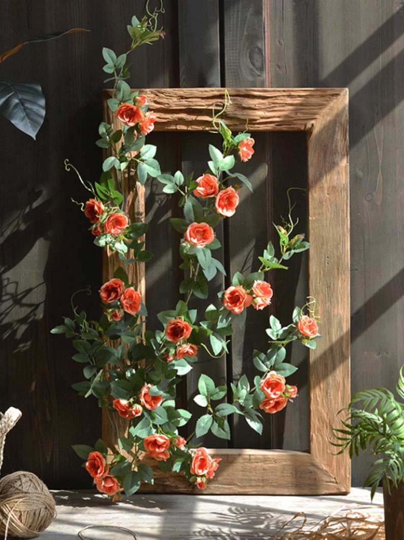 Puede incluir: Un marco de madera con una vid de rosas artificiales de color naranja y hojas verdes. El marco es r&uacute;stico y tiene un acabado de madera natural.
