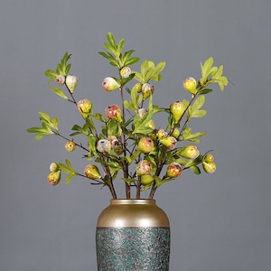 May include: A green ceramic vase with a gold rim holds a bouquet of artificial branches with small yellow and green fruit.