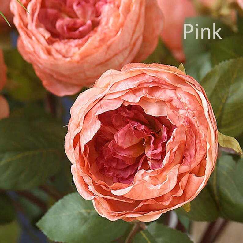 Puede incluir: Primer plano de una rosa artificial de color rosa con m&uacute;ltiples capas de p&eacute;talos. La rosa forma parte de un ramo de flores artificiales.