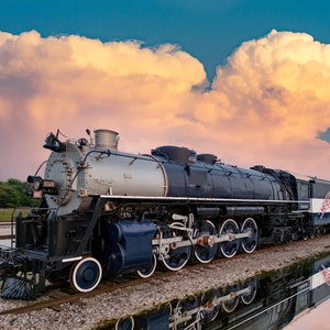 Peut inclure: Une locomotive à vapeur noire et argentée avec un logo "Meteor" rouge et bleu sur le côté, garée sur des voies ferrées avec un grand nuage moelleux en arrière-plan.