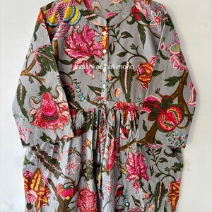 May include: A gray cotton dress with a floral print. The dress has a button-up front and a gathered waist. The print features pink, red, yellow, and green flowers on a gray background.