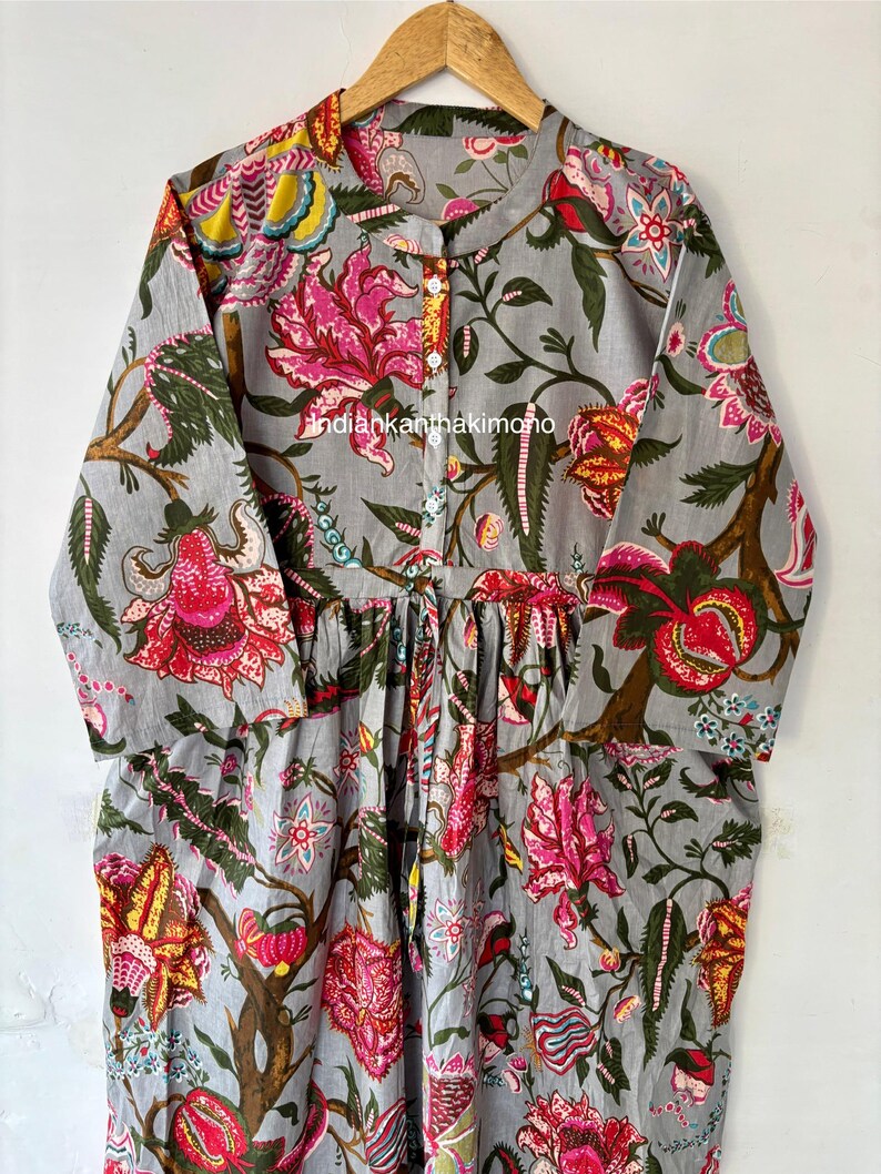 May include: A gray cotton dress with a floral print. The dress has a button-up front and a gathered waist. The print features pink, red, yellow, and green flowers on a gray background.