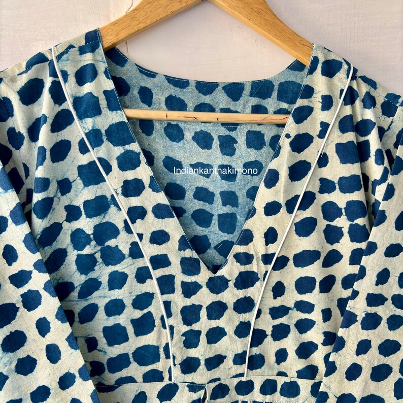 Puede incluir: Prenda de color crema con un patr&oacute;n repetitivo de formas irregulares de color azul oscuro. La prenda tiene un escote en V ribeteado con ribete blanco. El texto "indiankanthakimono" es visible.