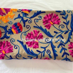 Puede incluir: Tela beige con bordado floral de colores. El bordado presenta flores rosas, azules, naranjas y amarillas. El texto "Indiankanthakkimono" es visible en el centro de la tela.