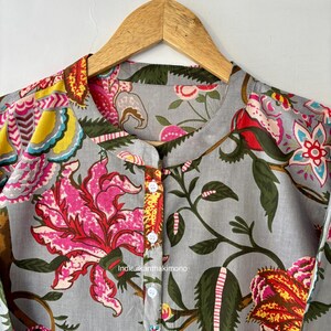 May include: A gray cotton shirt with a floral print in shades of pink, red, yellow, and blue. The shirt has a mandarin collar and a button closure. The text "indiakanthakimono" is printed on the shirt.