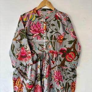 May include: A gray cotton dress with a floral print. The dress has a round neckline, long sleeves, and a button-up front. The floral print features pink, red, yellow, and green flowers.