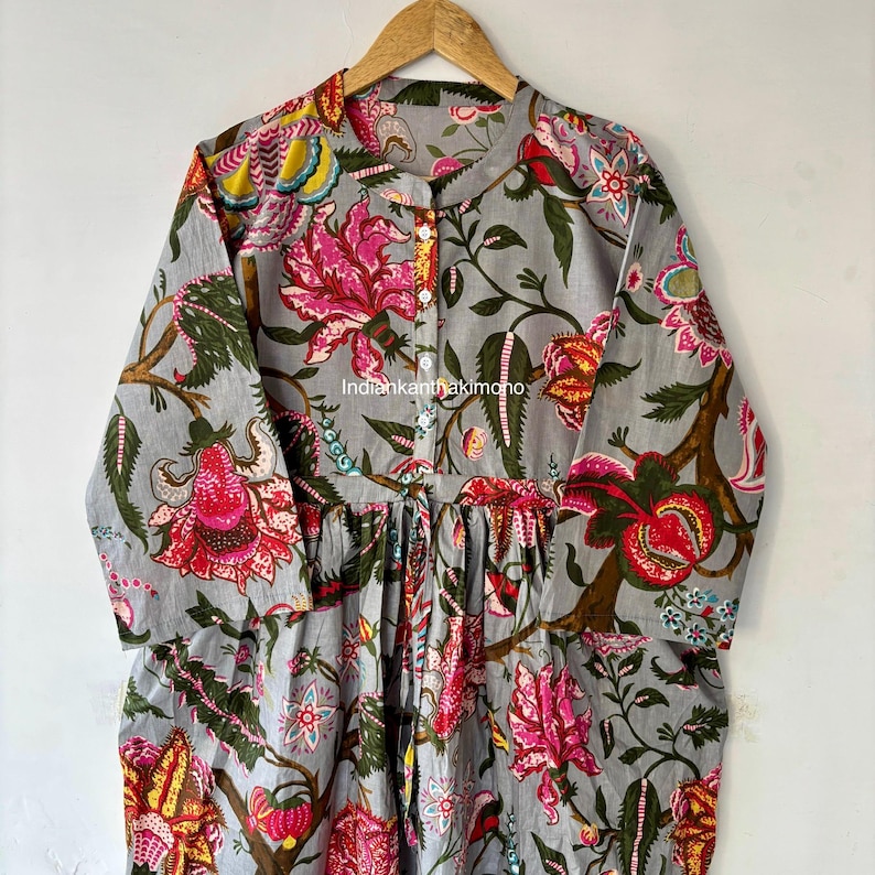May include: A gray cotton dress with a floral print. The dress has a round neckline, long sleeves, and a button-up front. The floral print features pink, red, yellow, and green flowers.
