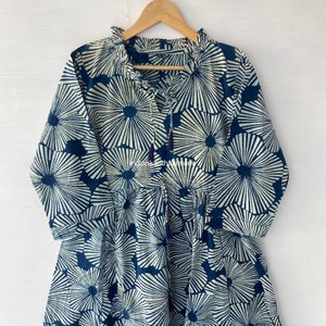 May include: A blue and white cotton dress with a floral print. The dress has a ruffled neckline and a tie at the front.