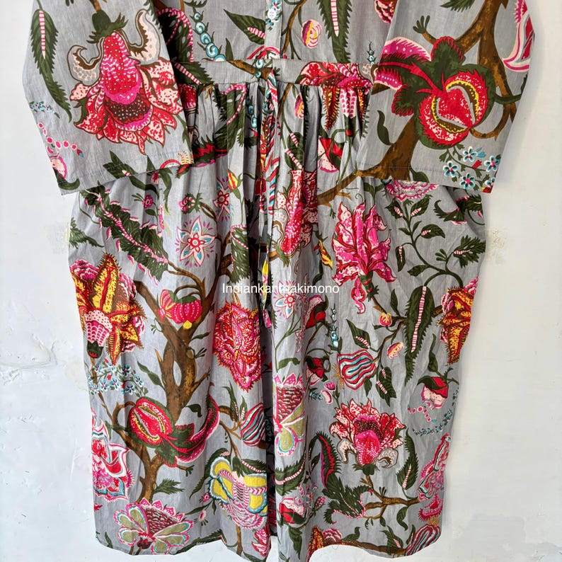 May include: A gray cotton dress with a floral print featuring pink, red, yellow, and green flowers. The dress has a button-up front and long sleeves.