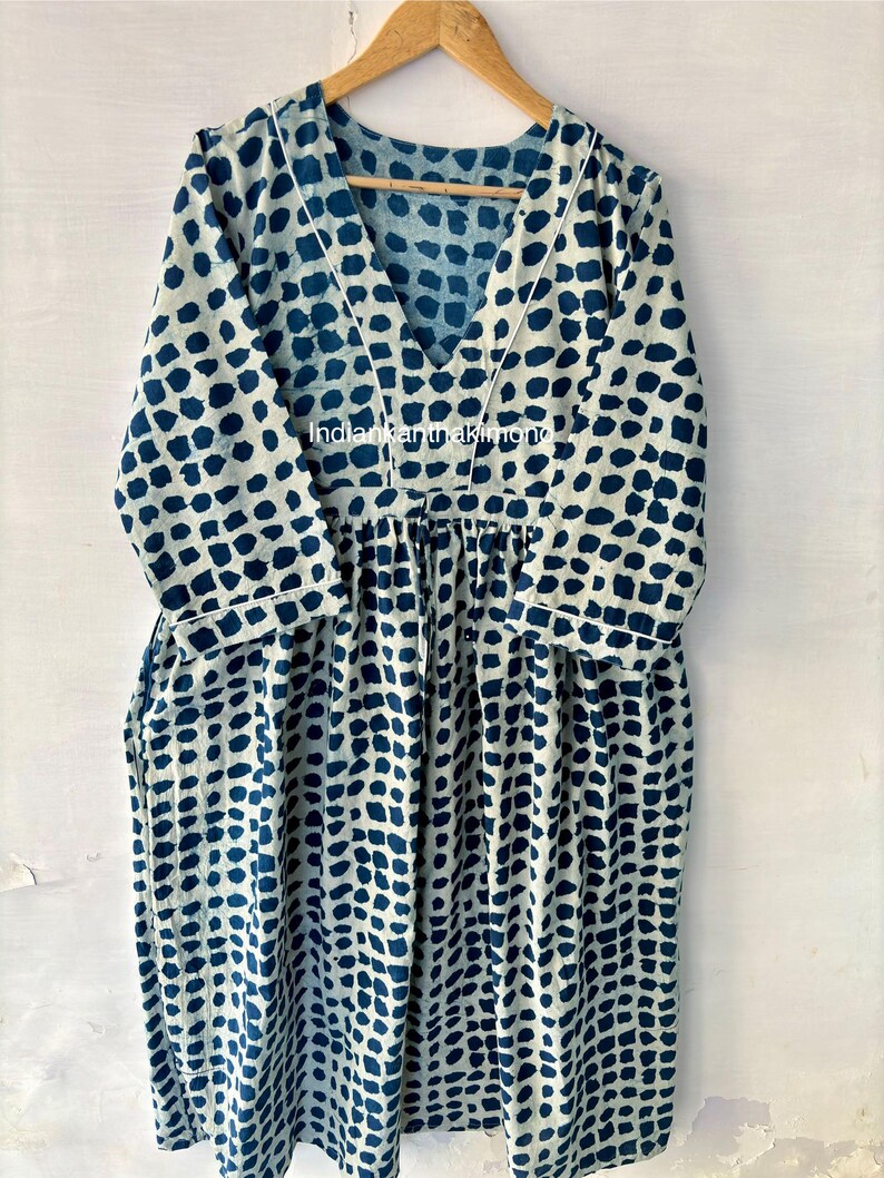 Puede incluir: Vestido de manga larga con cuello en V, con un estampado de puntos azul oscuro sobre fondo azul claro. El vestido est&aacute; colgado en una percha de madera. El texto "indiankanthakimono" es visible en el vestido.