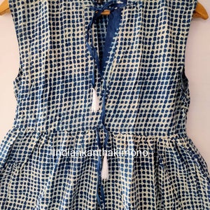 Könnte beinhalten: Ein ärmelloses blaues und weißes Kleid mit einer Schleife am Hals und weißen Quasten. Das Kleid hat ein Punkte-Muster.