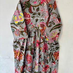 May include: A gray cotton dress with a floral print in shades of pink, yellow, green, and red. The dress has a gathered waist and long sleeves.