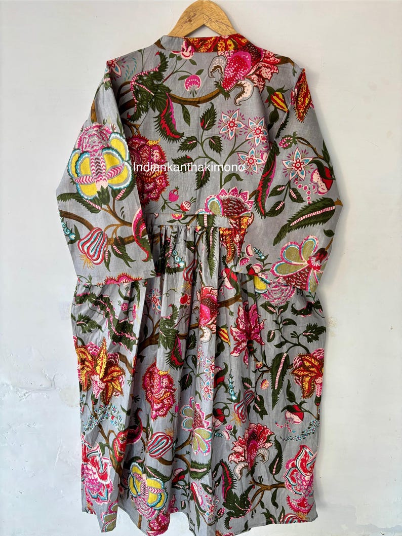May include: A gray cotton dress with a floral print in shades of pink, yellow, green, and red. The dress has a gathered waist and long sleeves.