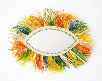 May include: A round mirror with a woven frame and colorful fringe. The fringe is in shades of green, yellow, orange, and blue.