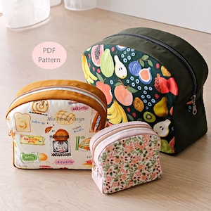 Puede incluir: Tres estuches con cremallera de diferentes tamaños. El más grande es verde oscuro con un estampado de frutas coloridas. El mediano es amarillo mostaza con un estampado de pan y panadería blanco con la etiqueta Miss Freckler Design. El más pequeño es rosa.