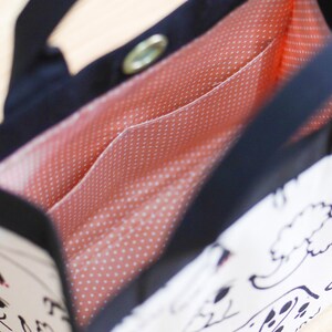 Pu&ograve; includere: Una borsa tote bianca e nera con una fodera a pois rossi e bianchi. La borsa ha un'unica tracolla e una chiusura a zip.