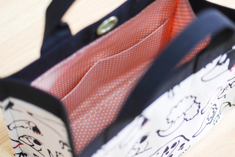 Pu&ograve; includere: Una borsa tote bianca e nera con una fodera a pois rossi e bianchi. La borsa ha un'unica tracolla e una chiusura a zip.