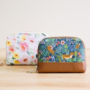 May include: Two small zippered pouches with different floral patterns. The pouch on the left has a white background with pink and yellow flowers. The pouch on the right has a blue background with green leaves, orange tigers, and pink flowers.