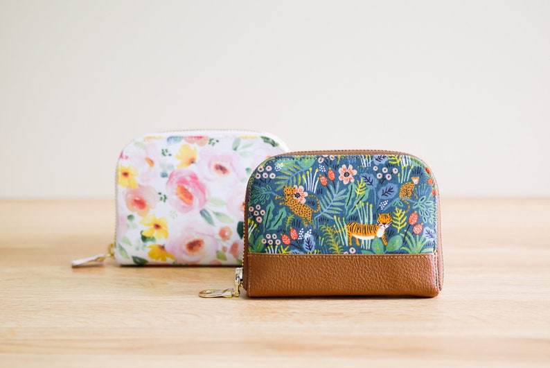 May include: Two small zippered pouches with different floral patterns. The pouch on the left has a white background with pink and yellow flowers. The pouch on the right has a blue background with green leaves, orange tigers, and pink flowers.