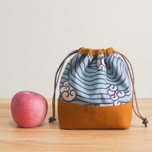 May include: A blue and brown drawstring bag with a wave and cloud pattern. The bag is made of fabric and has a leather bottom.
