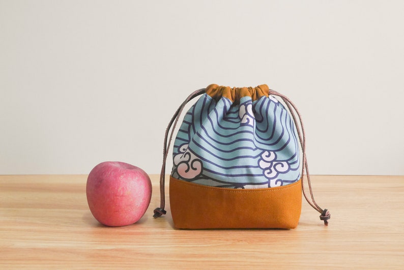May include: A blue and brown drawstring bag with a wave and cloud pattern. The bag is made of fabric and has a leather bottom.