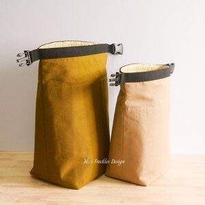 Pode incluir: Duas bolsas de enrolar com al&ccedil;as de tecido preto e fivelas de pl&aacute;stico. A bolsa maior &eacute; amarelo-mostarda e a menor &eacute; bege. Ambas possuem um forro interno claro e o texto Miss Freckles Design.