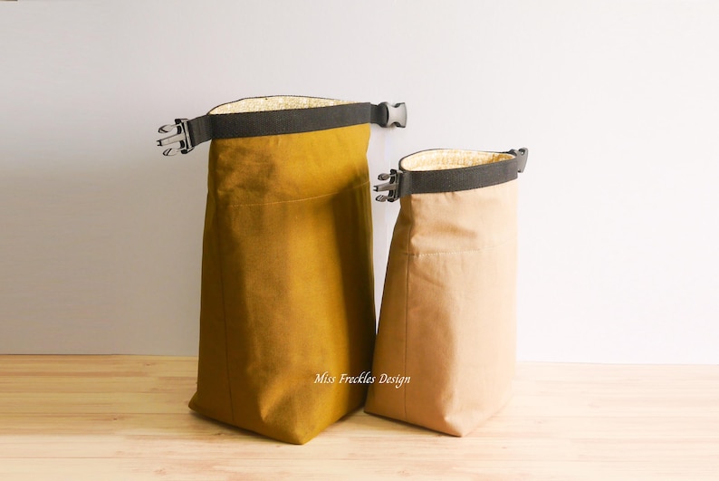 Pode incluir: Duas bolsas de enrolar com al&ccedil;as de tecido preto e fivelas de pl&aacute;stico. A bolsa maior &eacute; amarelo-mostarda e a menor &eacute; bege. Ambas possuem um forro interno claro e o texto Miss Freckles Design.