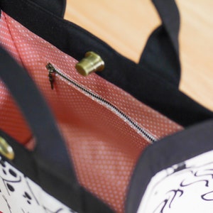Pu&ograve; includere: Una borsa tote bianca e nera con una fodera a pois rosa. La borsa ha una tasca con cerniera e un manico superiore.