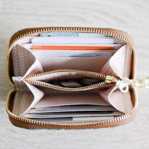May include: A small, brown zippered wallet with a colorful floral pattern. The wallet is open and shows multiple card slots and a zippered compartment.