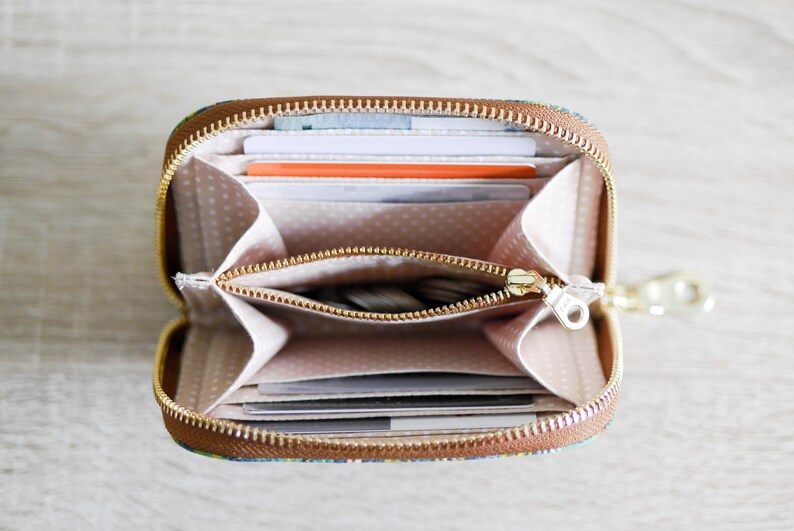 May include: A small, brown zippered wallet with a colorful floral pattern. The wallet is open and shows multiple card slots and a zippered compartment.