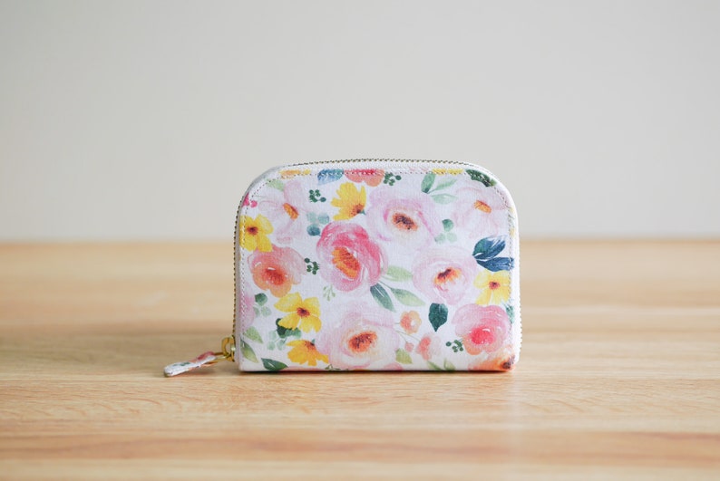 May include: A white zippered pouch with a floral print featuring pink, yellow, and green flowers.