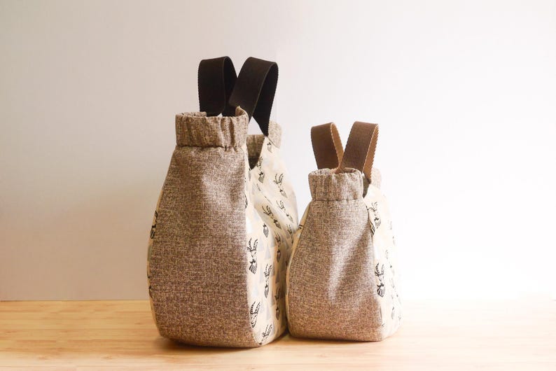 May include: Three fabric bags with brown handles. The bags are different sizes and have a textured, light brown fabric on the front and back. The middle bag has a cream-colored fabric with a black pattern.