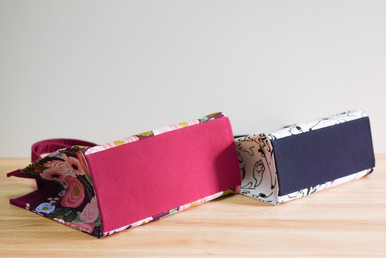 Pu&ograve; includere: Due borse tote con motivi diversi. La borsa a sinistra ha un motivo floreale con fiori rosa, bianchi e verdi su uno sfondo bordeaux. La borsa a destra ha un motivo bianco e nero con forme astratte. Entrambe le borse hanno un fondo di colore pieno.